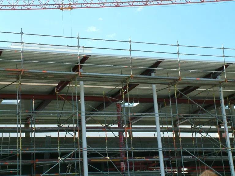 Rohbau eines langgestreckten Multiplexgebäudes mit eingerüsteter Fas - Ingenieurbüro Makowka & Hanik Rohbau eines langgestreckten Multiplexgebäudes mit eingerüsteter Fassade und weit auskragendem Vordach vor blauem Himmel