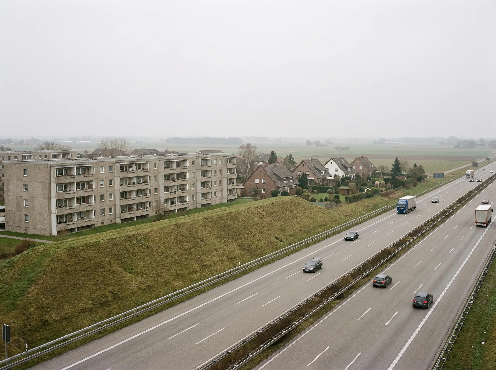 Autobahn mit Lärmschutzwall und abschirmender Wohnbebauung (KI-Visualisierung, Symbolbild) - Ingenieurbüro Makowka & Hanik Visualisierung einer Autobahn mit begrüntem Lärmschutzwall, dahinter eine geschlossene Wohnzeile und im Lärmschatten niedrigere Einfamilienhäuser